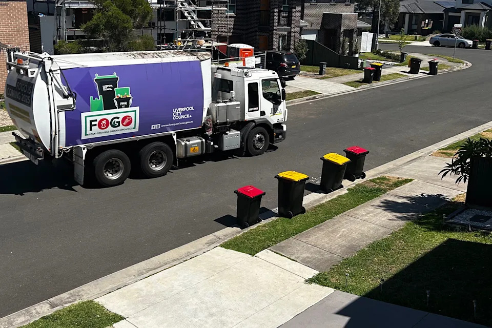 A garbage truck on a suburban Aussie street that has bins lining the sides. 