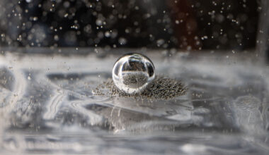 Tiny silver ball bearings crowd around a larger bearing in a clear, viscous fluid. Some of the smaller ball bearings are suspended in the fluid.