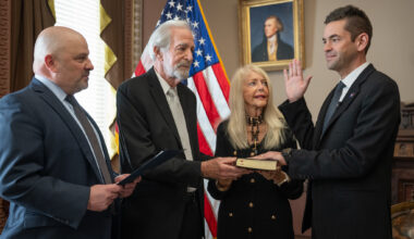 Four people, including NASA Administrator Jared Isaacman, stand in an office with an American flag in the background, as Isaacman is sworn in, with his right hand raised.