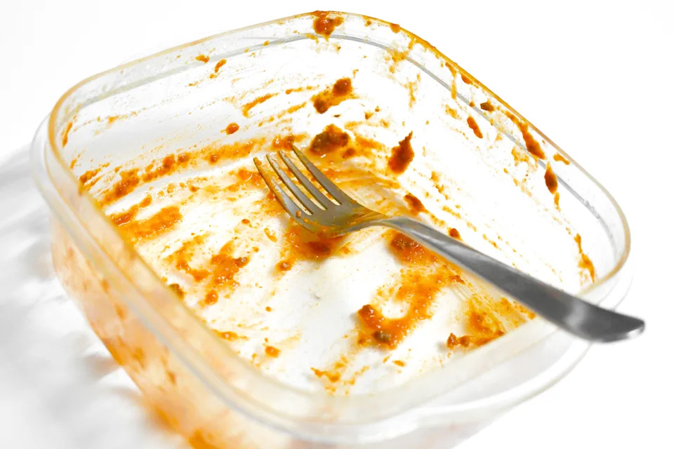 Empty plastic container with sauce remnants and a fork inside