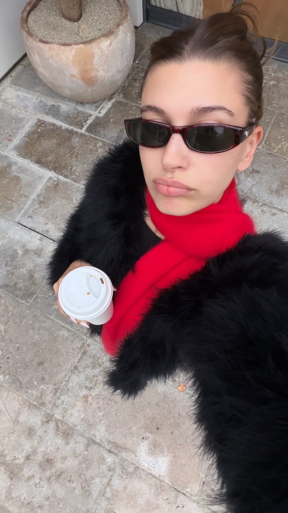 person holding a coffee cup while wearing a black fur coat and red scarf