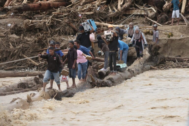Flood survivors use logs to cross a river in Batang Toru, North Sumatra, Indonesia, on Dec. 2, 2025. Image by AP Photo/Binsar Bakkara.