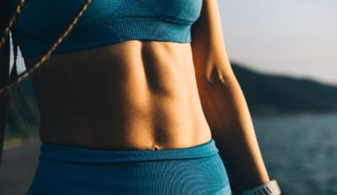 A close-up of a woman's athletic torso, showing her toned abs and a blue sports bra. Wearable health tracker on the hand. The golden hour sunlight highlights the muscles and fabric, creating a powerful image that represents fitness goals, body confidence, and strength.
