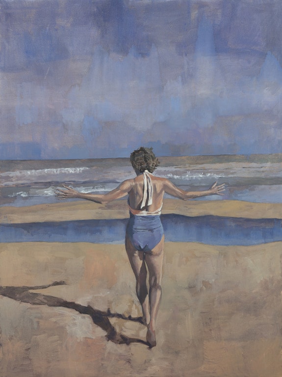 Woman in a blue swimsuit walking towards the ocean on a sunny beach day, arms outstretched, under a blue sky.