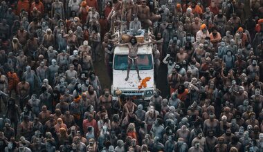 Aerial view of a large congregation of people covered in ash and paint, grouped around a vehicle, engaged in a vibrant spiritual gathering