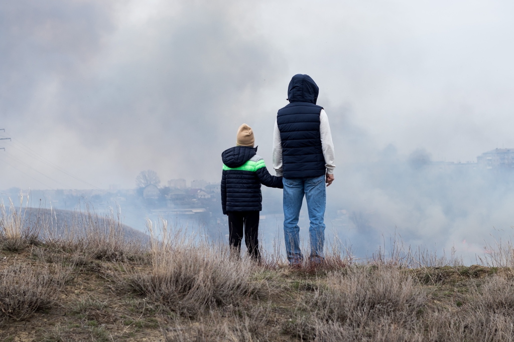 For the first time, researchers at OHSU evaluated the long-term impact of air pollution on adolescent brain health and development. (Getty IMage) A woman and child holding hands on top of a grassy hill, looking down on wildfire damage and smoke.