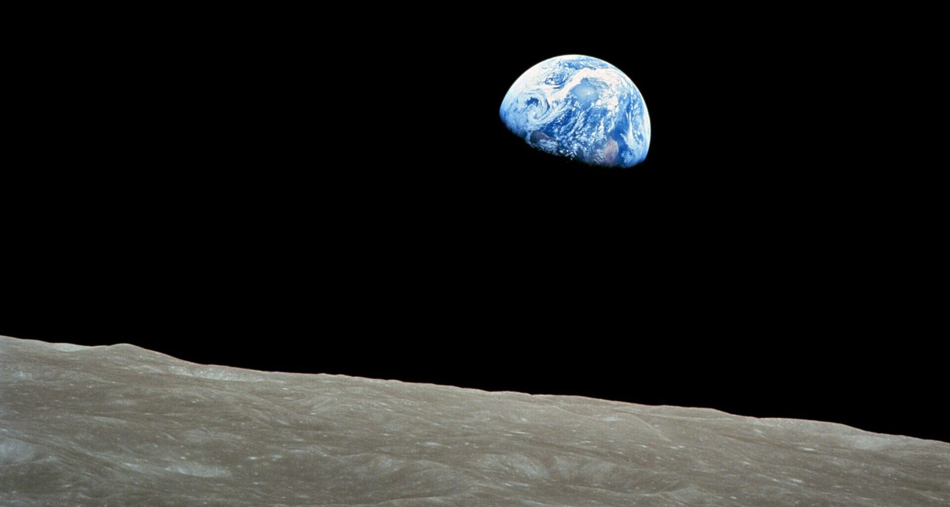 A photo of the Earth in the darkness of space with the surface of the moon in the foreground of the image