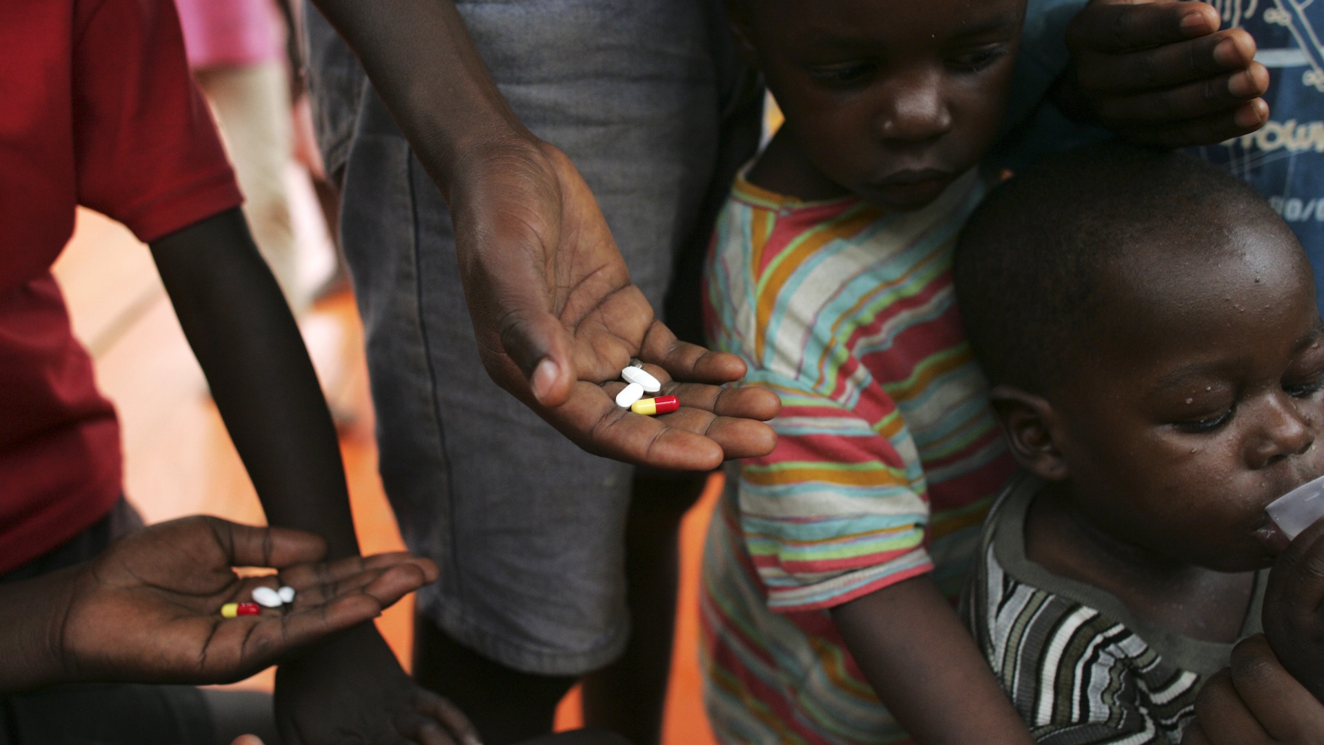 A group of Ugandan adults and children stand with HIV medication in their hands