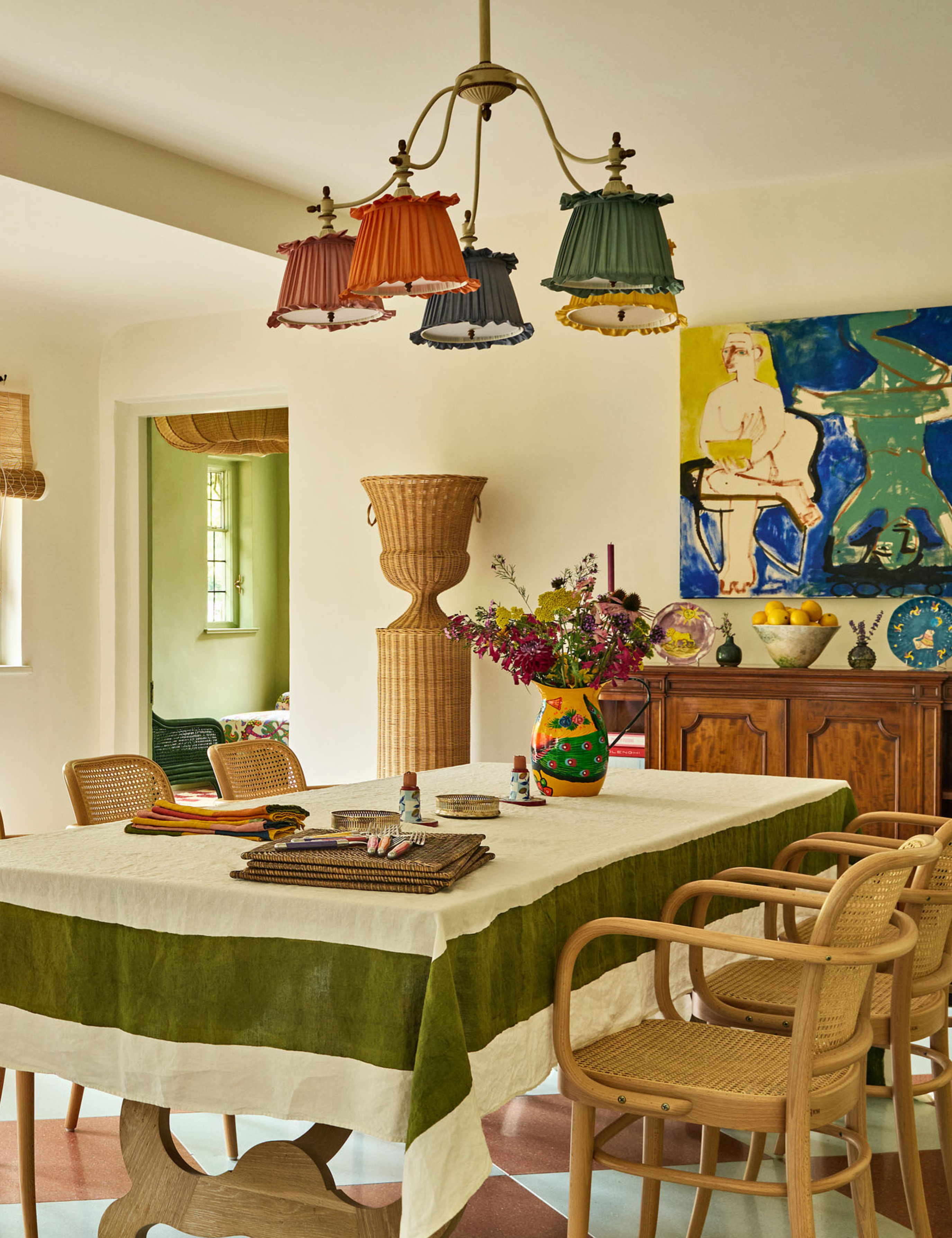 Colorful sundrenched dining room featuring an antiqued wooden table covered by a green bordered tablecloth and a collection of colorful tableware.