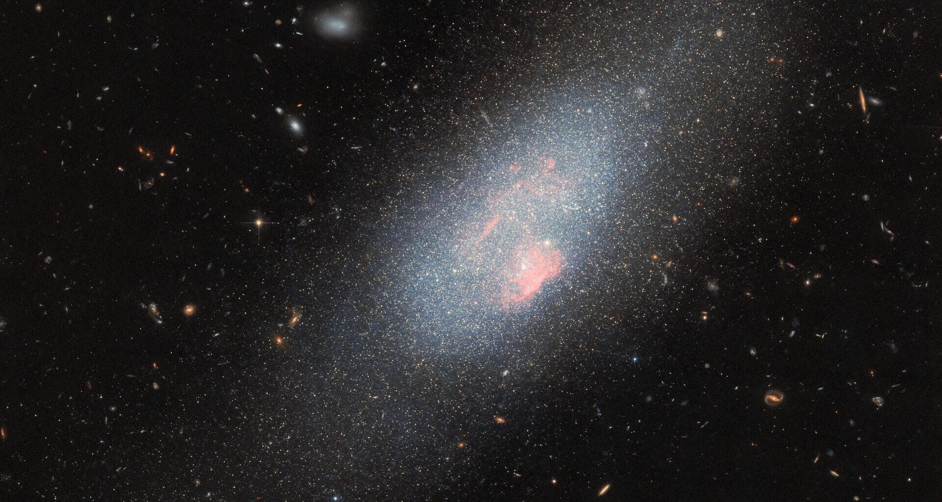 A glowing swirl of lights surrounds denser areas of pink color with stars surrounding the galaxy in a deep space image.