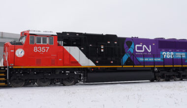 Red, white, and black locomotive with purple section of long hood and logo of 988 Lifeline