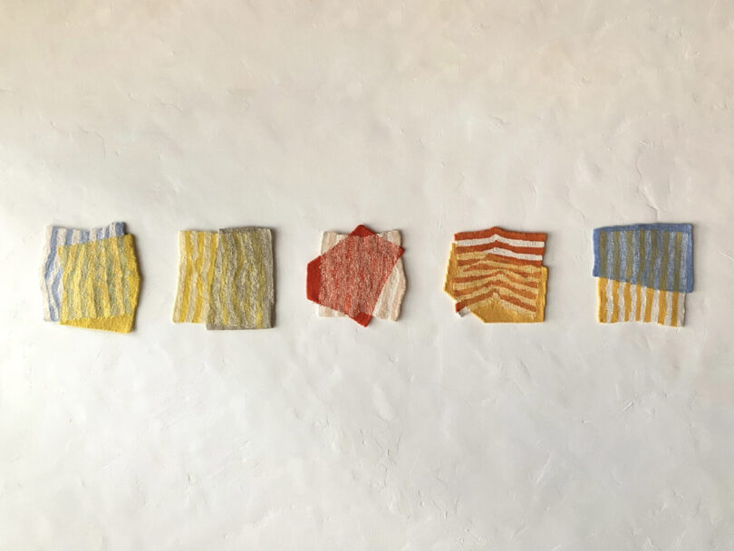 Five textured, square fabric swatches in different colors and striped patterns—are evenly spaced in a horizontal row against a plain off-white wall.