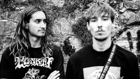 Torus Two young men, one on the left with long hair and one on the right with shorter hair and a light beard, shot in black and white