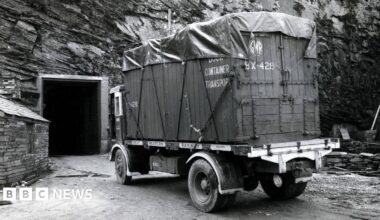 A black and white image of a container truck seen outside a door