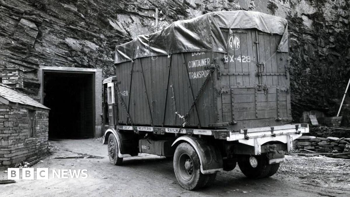 A black and white image of a container truck seen outside a door