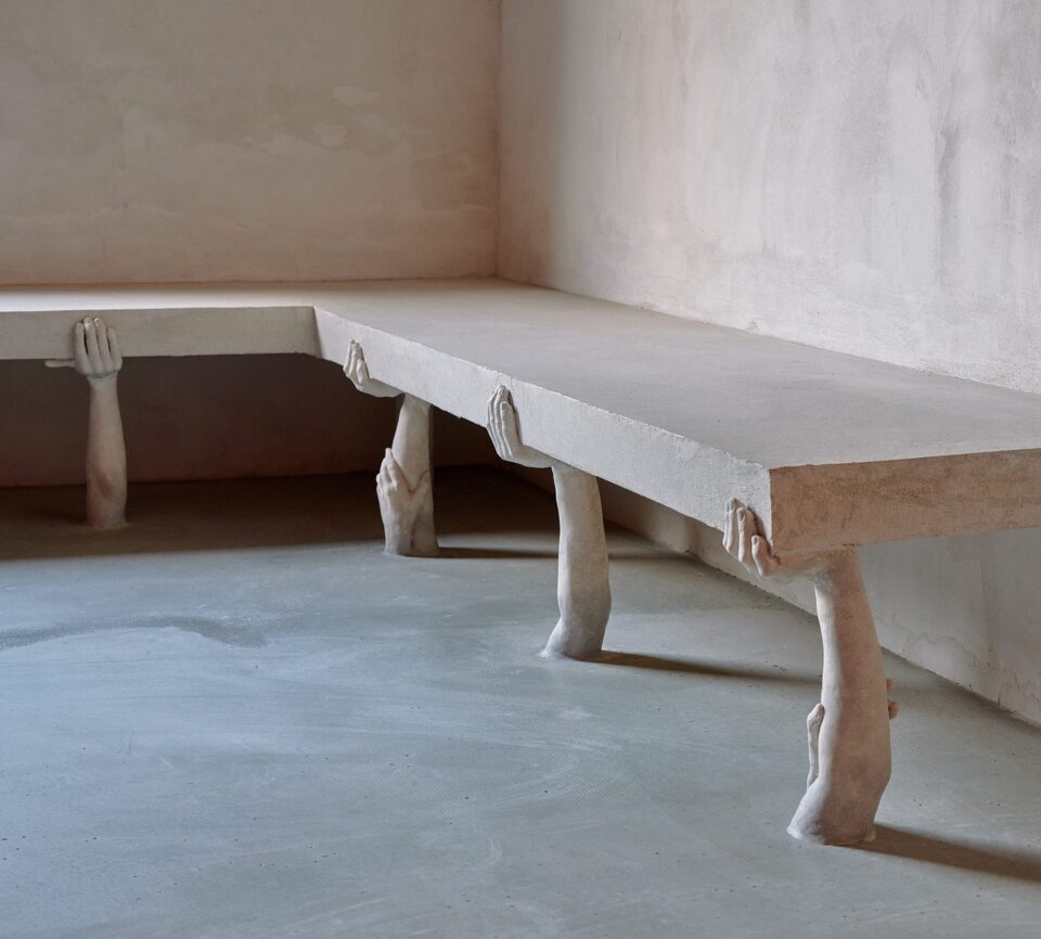 An art installation by Clementine Keith-Roach and Christopher Page of a bench with legs shaped like hands holding up the seats