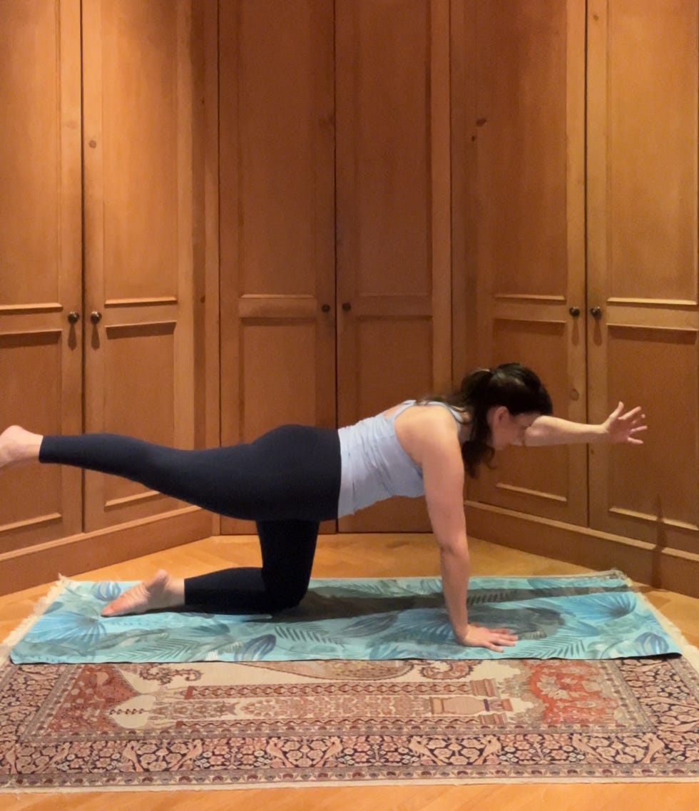 a person performing an exercise on a mat in a room with wooden cabinetry.