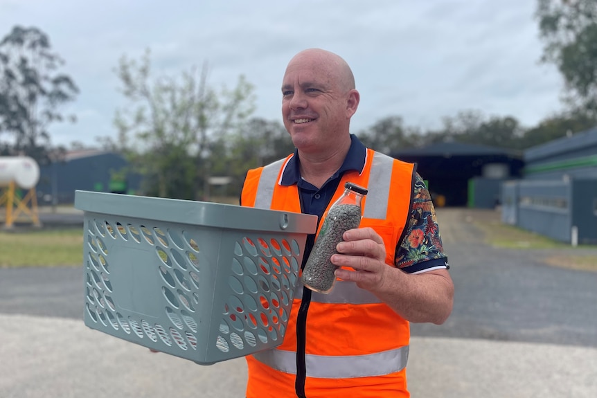 A man stands holding grey pellets, and a container made with recycled plastic.