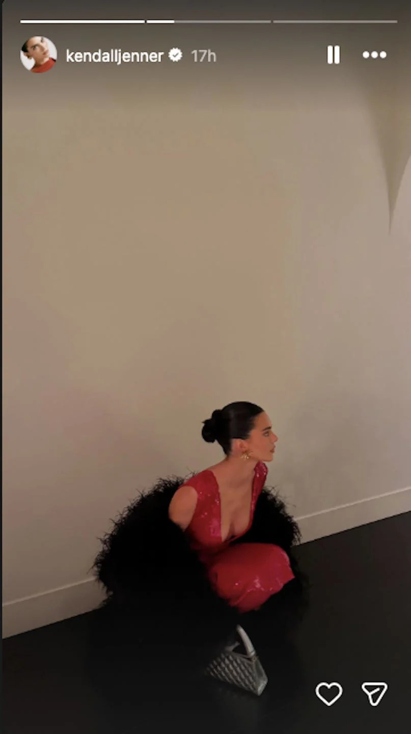 a person wearing a red dress and black shawl sitting against a wall