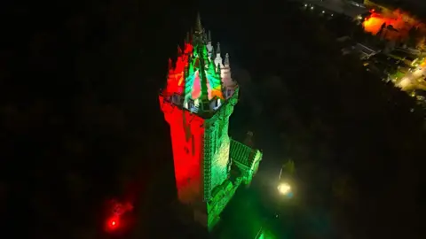 Kevin Hamill A large tower taken from a drone. The tower is lit up in green and red