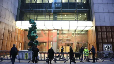 PA Media Police officers and security staff standing behind barriers outside an office building on Fenchurch Street, with red paint visible on the glass frontage following an early-morning protest.