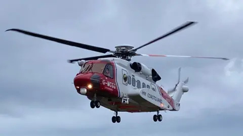 BBC A red and white coastguard helicopter photographed against a dark grey sky