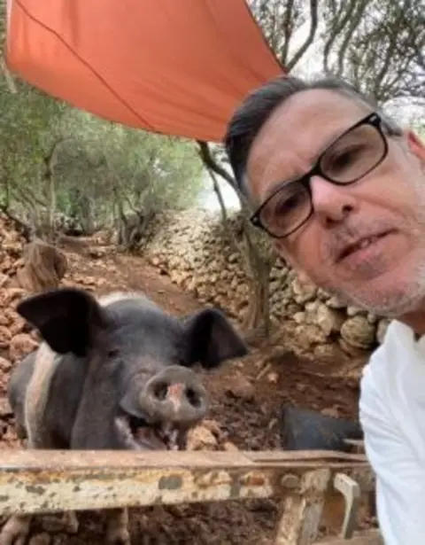 Menorca Donkey Rescue A man with glasses and a white top. A large pig appears to be smiling in the background.