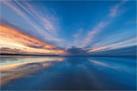 Alan Butterfield A blue and orange sky reflected in the water at at a beach