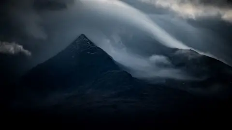 Jez Campbell A very dark picture of a mountain surrounded by clouds
