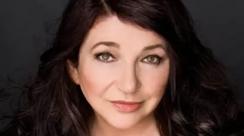 AFP Kate Bush smiling at the camera. She has dark brown hair and eyes.