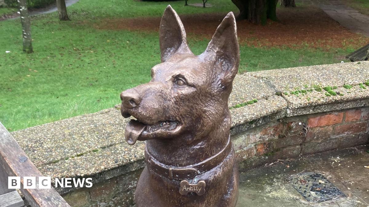 A wooden bench with the engraved words “HOPE IS EVERYTHING” on the seat is next to a bronze statue of a German shepherd dog.