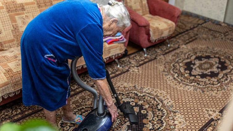 An older woman bends over as she vacuums her carpet.