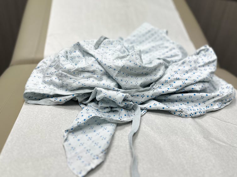 A rumpled medical gown with a light-blue print sits on top of an examining table.