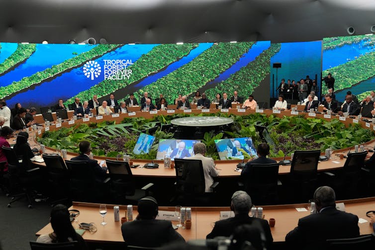 A group of delegates sit around a round table with forest images in the background.