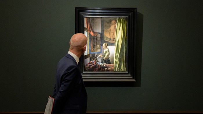 A man in a suit looks at Johannes Vermeer’s painting "Girl Reading a Letter at an Open Window" displayed in a gallery.