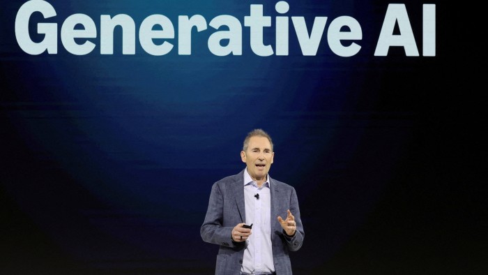 Andy Jassy speaks on stage in front of a large screen displaying the words “Generative AI.”