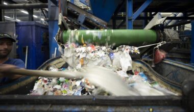 A worker moves a shovel while paper and plastic labels are processed on a conveyor at a recycling facility.