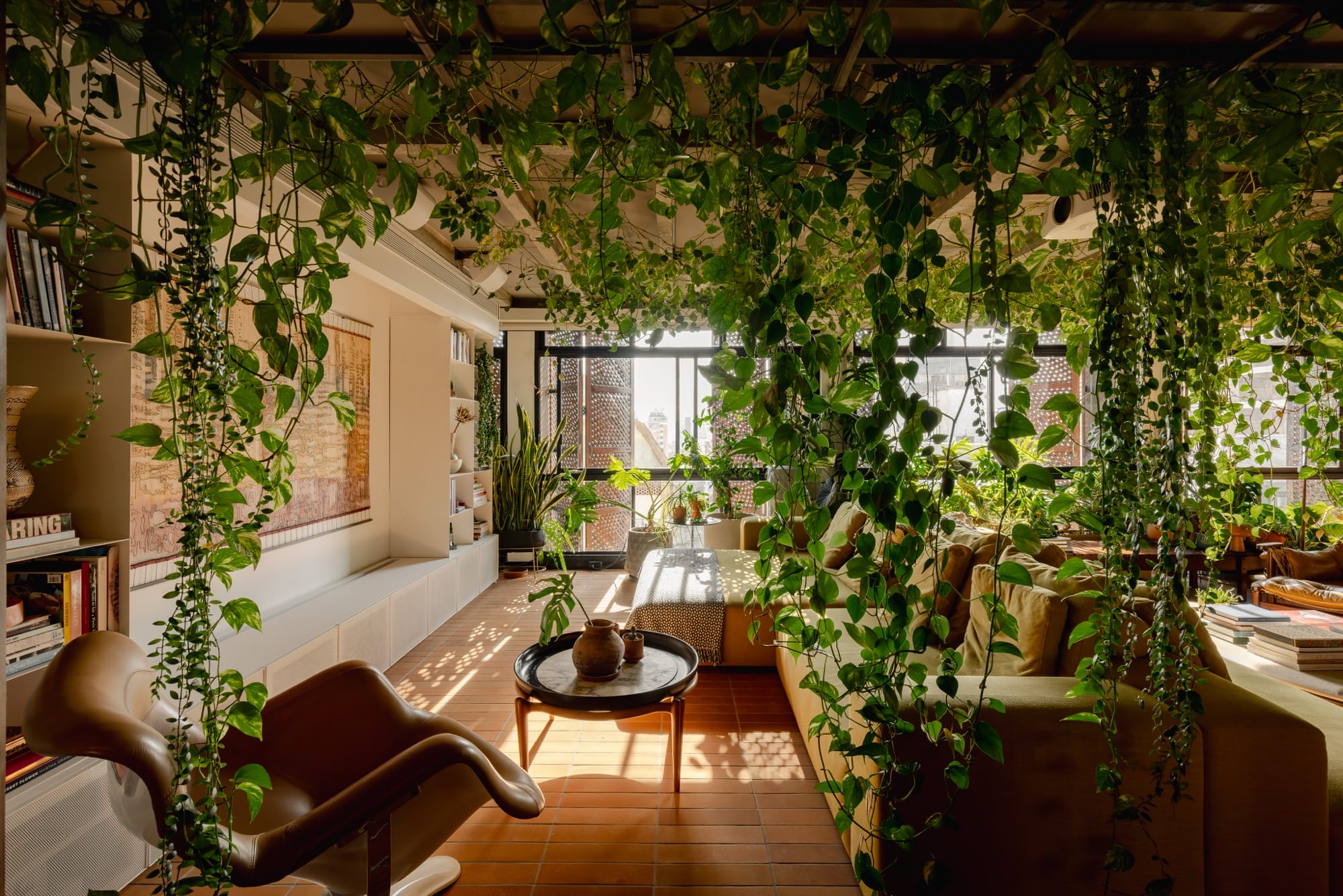 An apartment interior designed by Guto Requena with an eclectic variety of contemporary furnishings and houseplants draping from rafters in the ceiling