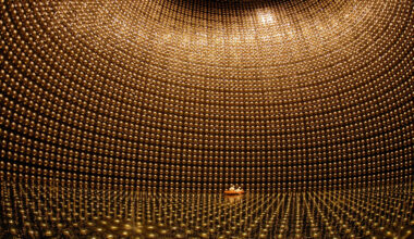 Two people sit in a boat inside of a large room with spherical objects surrounding them.
