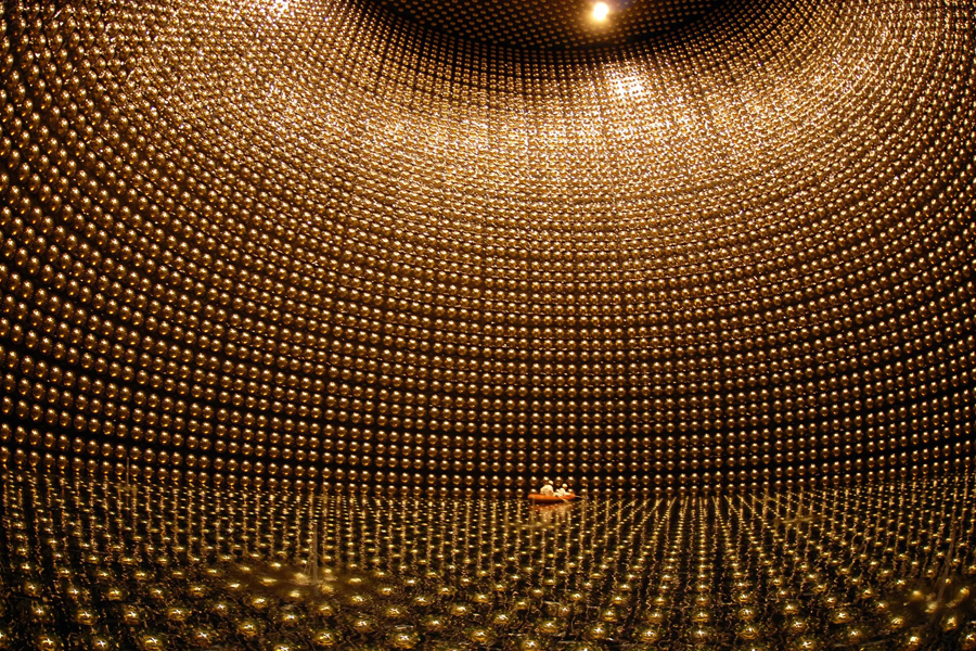 Two people sit in a boat inside of a large room with spherical objects surrounding them.