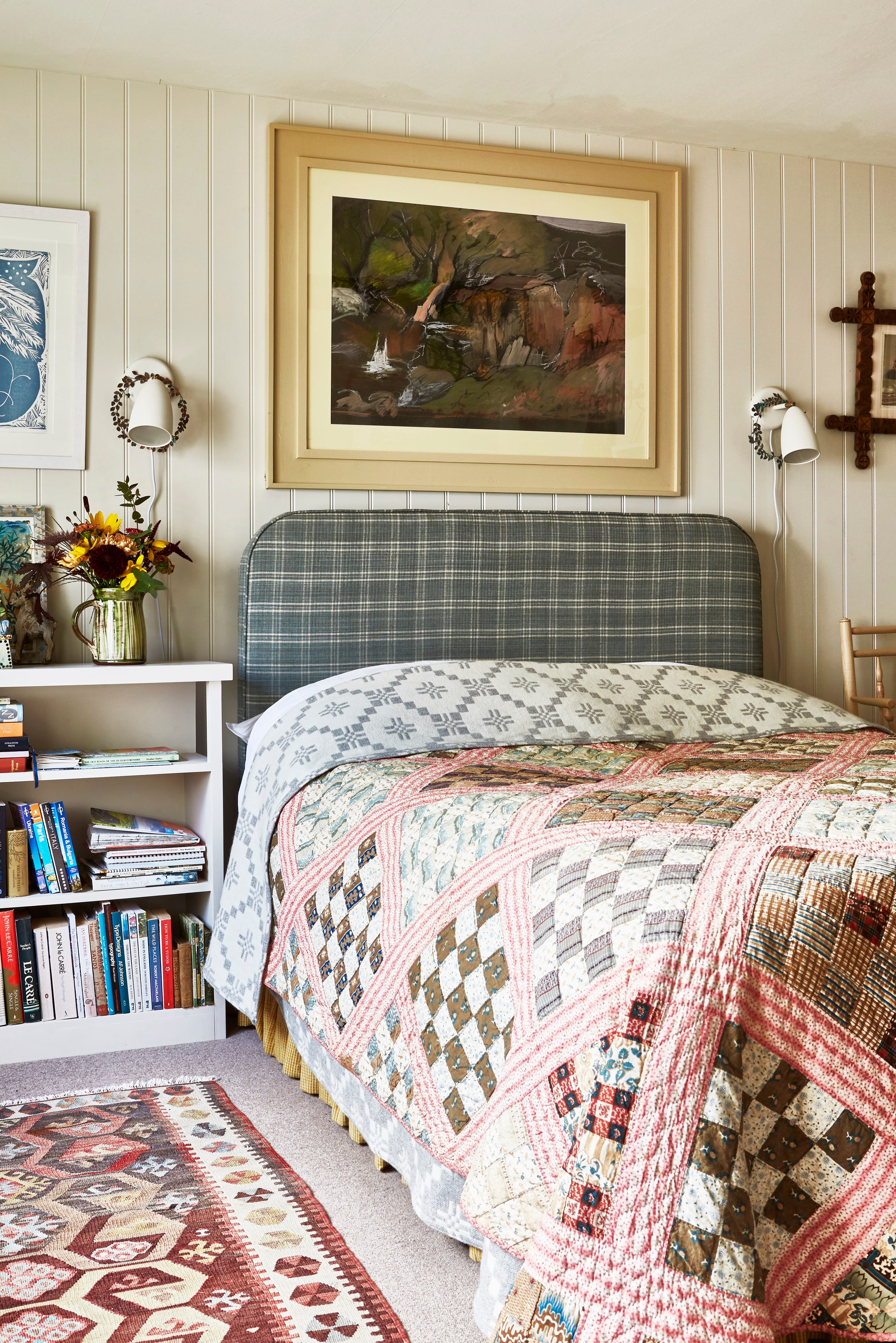 larger bedroom with patchwork quilt, melin tregwynt blanket and bookshelves built into a white panelled wall