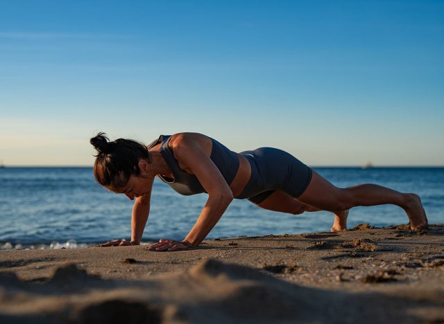 Athletic woman doing push ups on sandy beach in morning sunlight