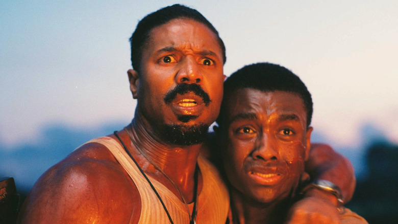 Michael B. Jordan as Smoke Moore and Miles Caton as Sammie look at a burning bar in Sinners