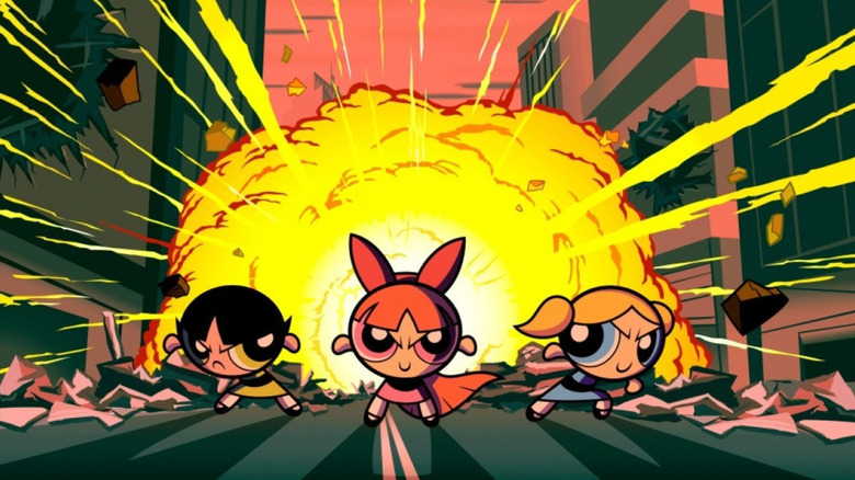 Buttercup (E.G. Daily), Blossom (Cathy Cavadini), and Bubbles (Tara Strong) stand in front of an exploding city street in The Powerpuff Girls