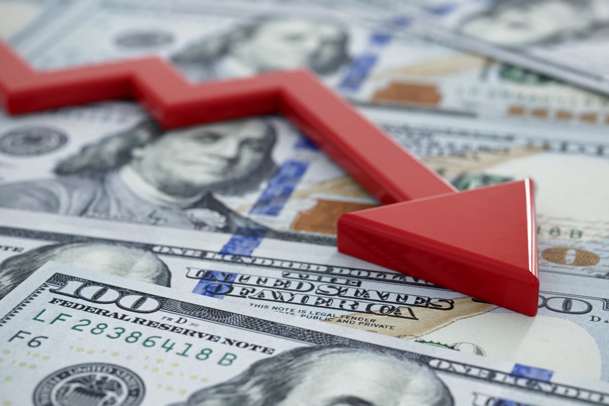 A downward-moving red arrow atop U.S. currency.