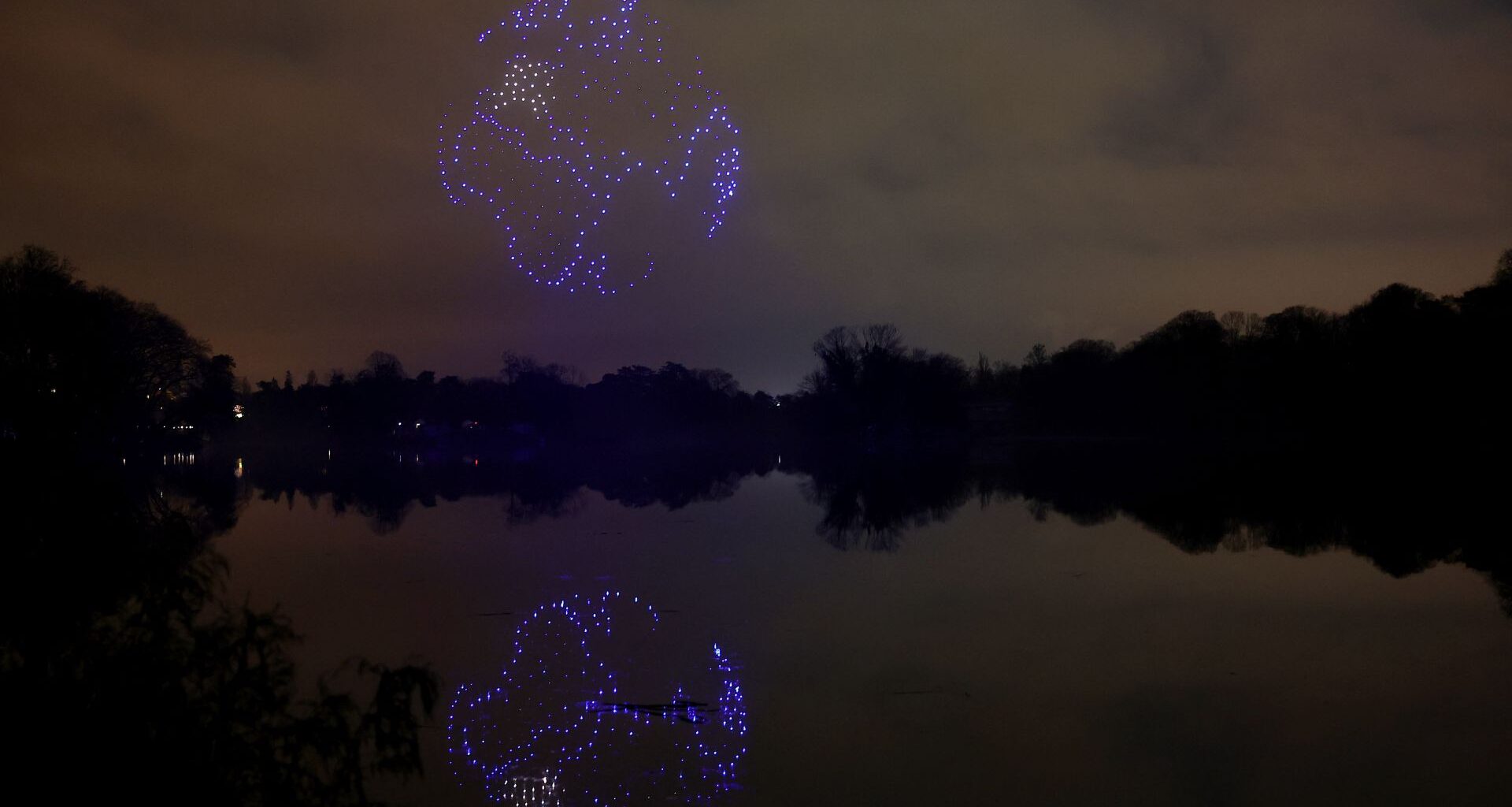 A series of purple drones come together in the night sky above a still lake to create a 3D image of planet Earth with the continent of Africa seen and reflected in the lake