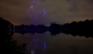 A series of purple drones come together in the night sky above a still lake to create a 3D image of planet Earth with the continent of Africa seen and reflected in the lake