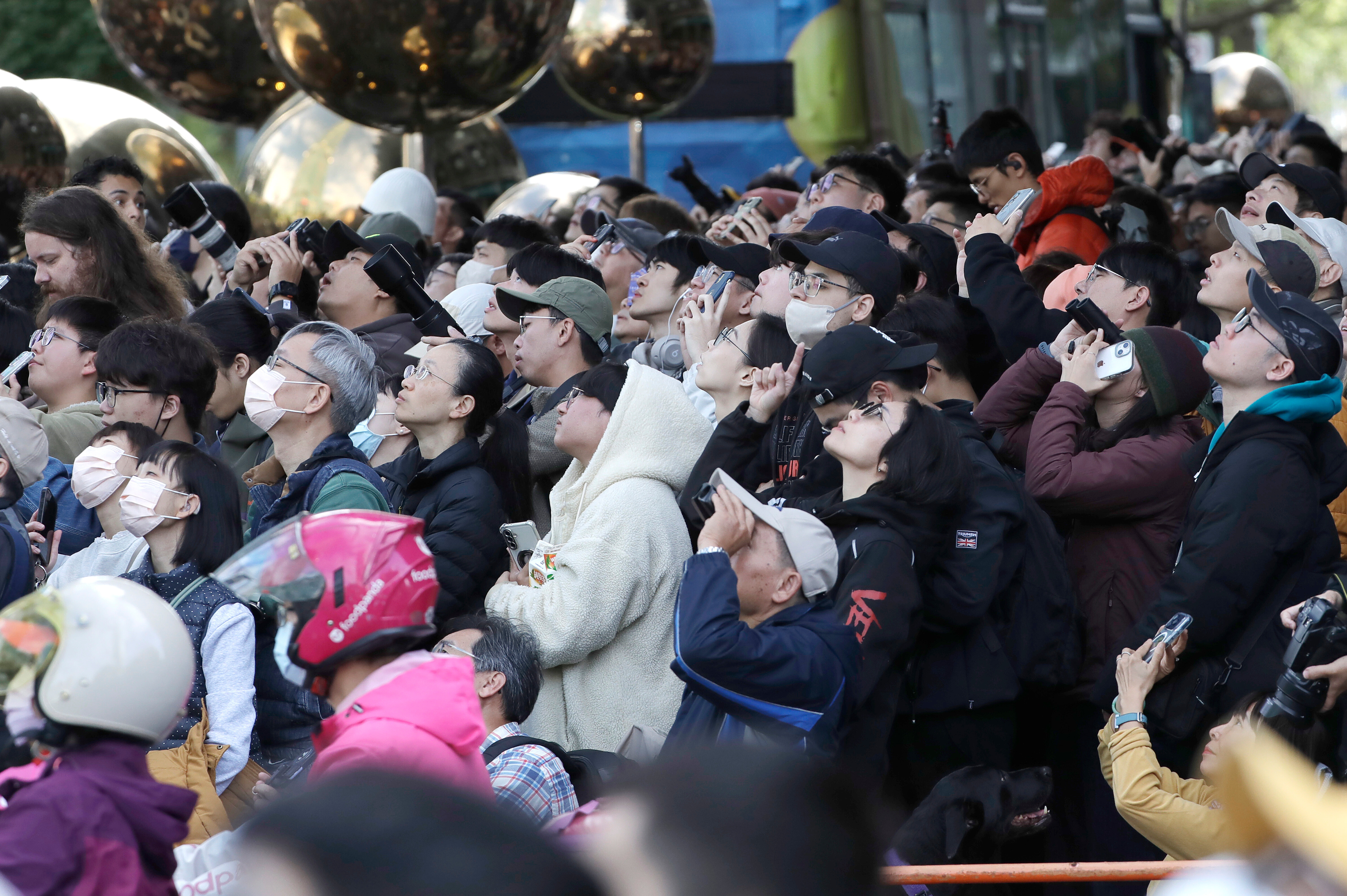 Crowd of people looking up, many holding phones to take pictures or videos.