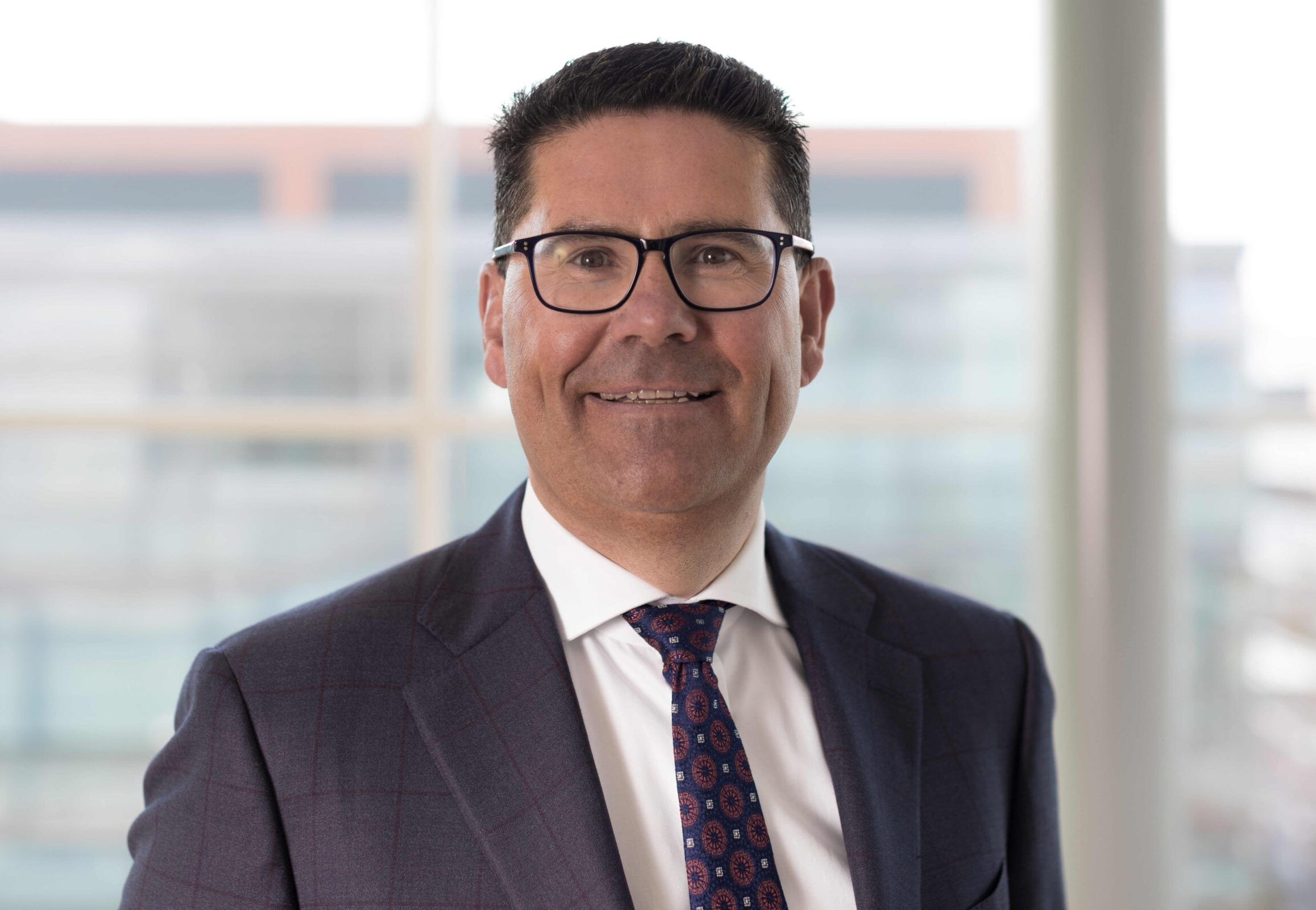 Joe Barrett, CEO of Applegreen, wearing a suit and tie and glasses.