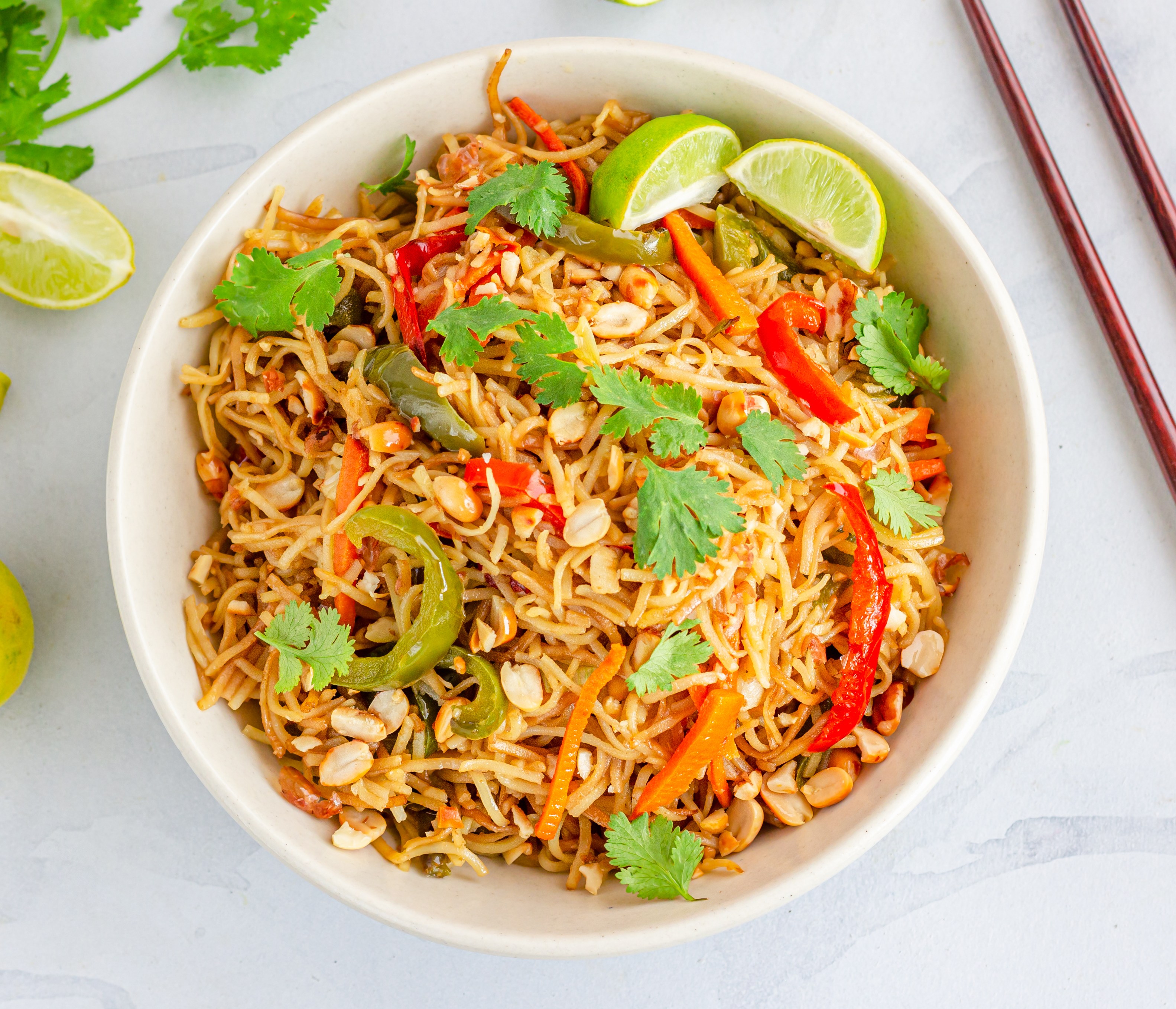 Thai Peanut Noodles with Vegetables, garnished with cilantro and lime, with chopsticks on the side.